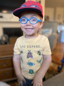 Young boy with Kniest and the world's biggest smile. He is wearing a red spider man hat and a 'bug expert' shirt.